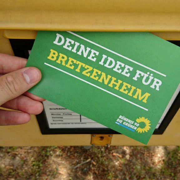 Eine grüne Postkarte mit der Aufschrift "Deine Idee für Bretzenheim" wird in einen Briefkasten eingeworfen.